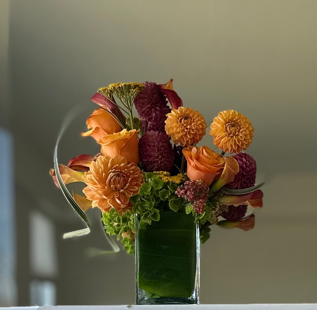 Bouquet of flowers in a clear vase on a reflective surface with a neutral background
