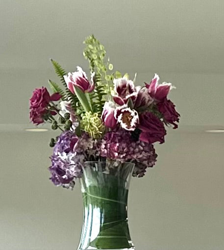 Bouquet of purple and green flowers in a clear vase on a light gray background