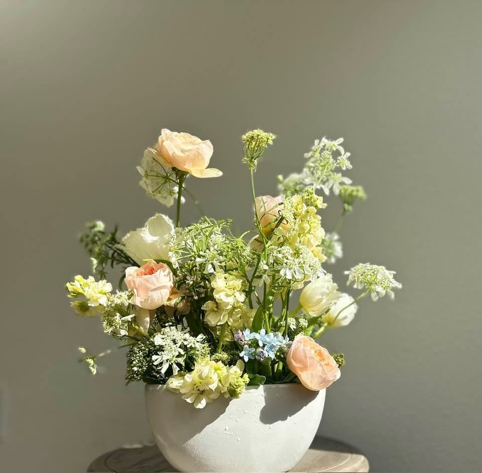 Bouquet of pastel flowers in a white oval vase against a plain background