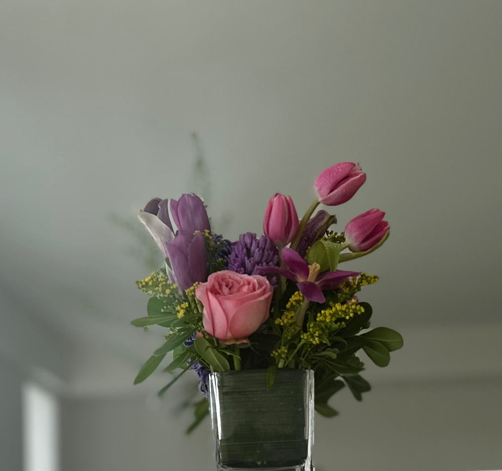 Bouquet of pink and purple flowers in a clear vase against a plain background